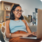 A woman sits at home on a sofa and uses a laptop. 